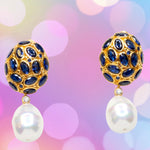 Pair of gold colored earrings with blue crystal and pearl like drop accents on a pastel multi-color background