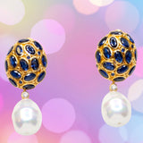 Pair of gold colored earrings with blue crystal and pearl like drop accents on a pastel multi-color background