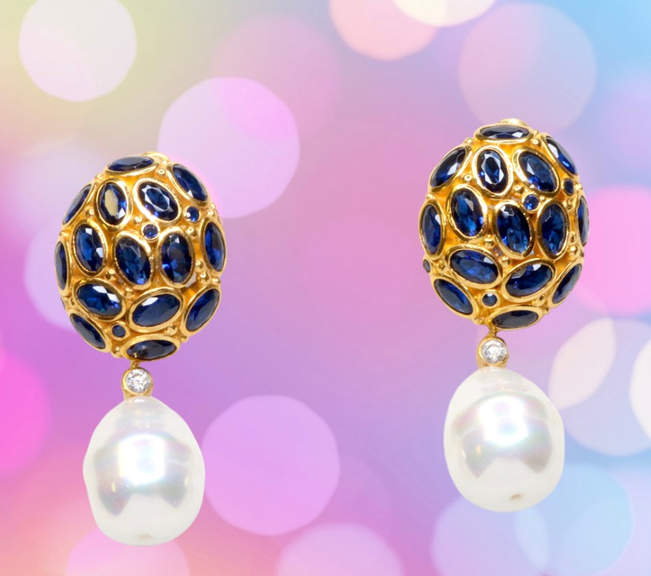 Pair of gold colored earrings with blue crystal and pearl like drop accents on a pastel multi-color background