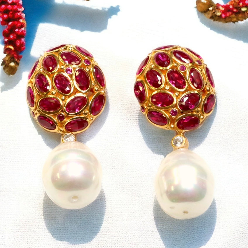 Pair of earrings with dark magenta crystals and pearl like drop accents on a white fabric background