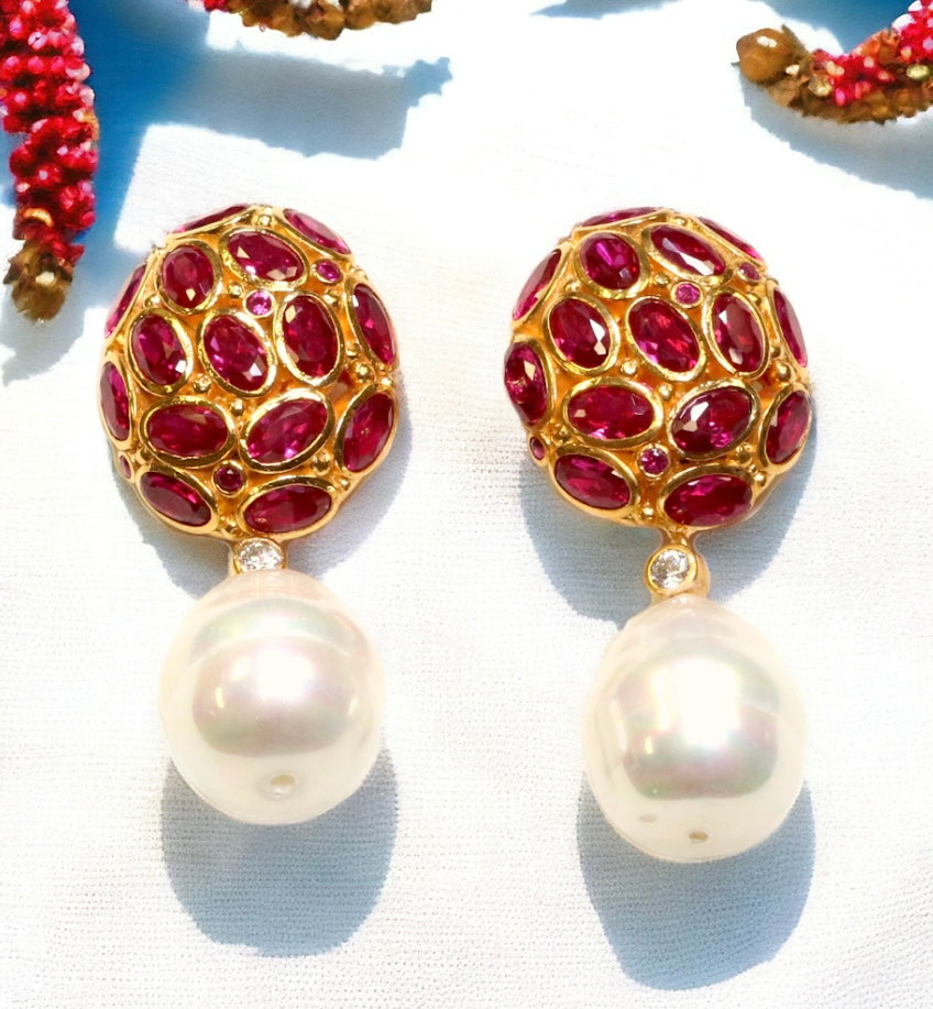 Pair of earrings with dark magenta crystals and pearl like drop accents on a white fabric background