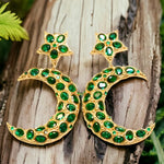 Gold colored moon and star shaped earrings with green crystal accents on a wooden background