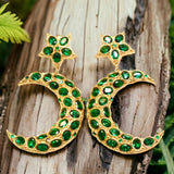 Gold colored moon and star shaped earrings with green crystal accents on a wooden background