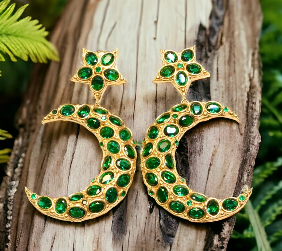 Gold colored moon and star shaped earrings with green crystal accents on a wooden background