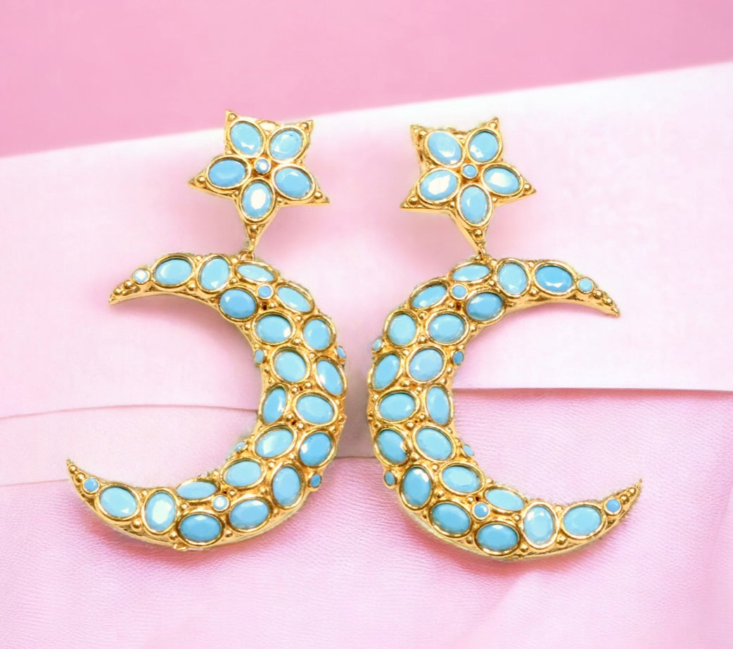 Gold and turquoise colored moon and star shaped earrings on a pink fabric background