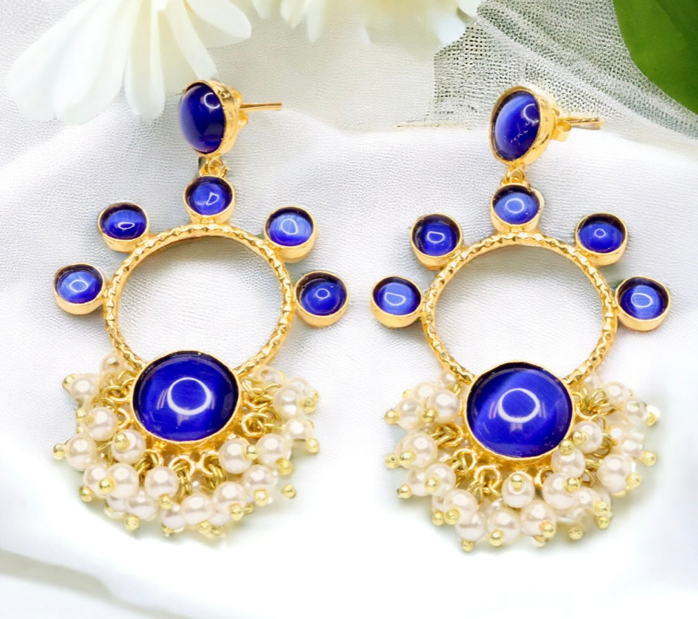 Gold earrings with blue stones and pearl-like accents on a white fabric background