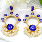 Gold earrings with blue stones and pearl-like accents on a white fabric background