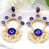 Gold earrings with blue stones and pearl-like accents on a white fabric background