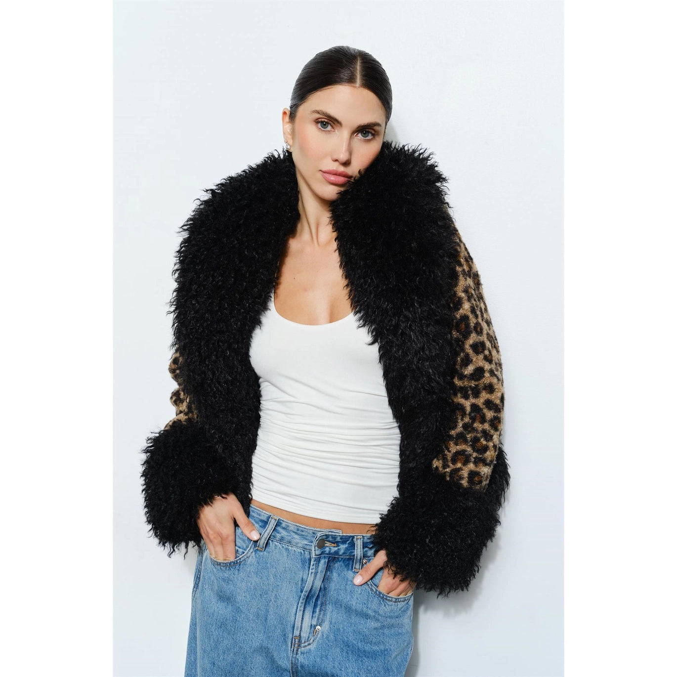 Woman wearing a leopard print coat with black faux fur trim on a white background with hands in her pockets