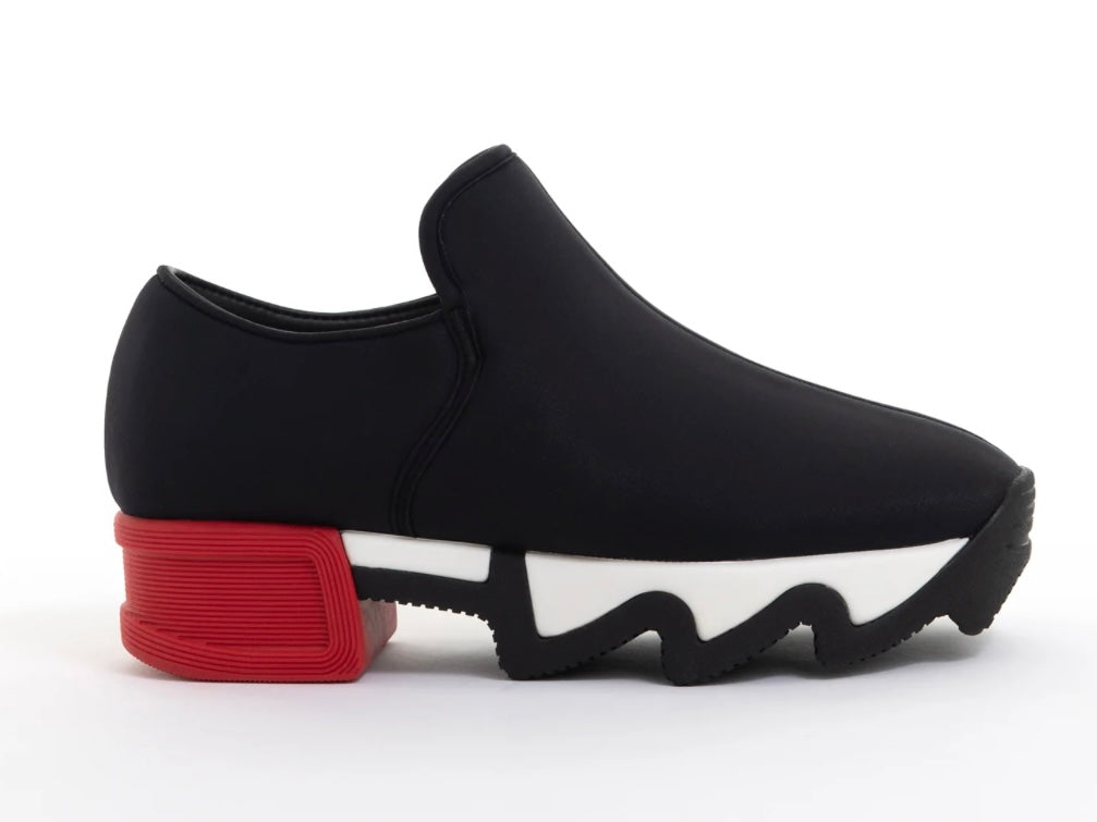 Black slip-on shoe with a red heel and black & white sole close-up