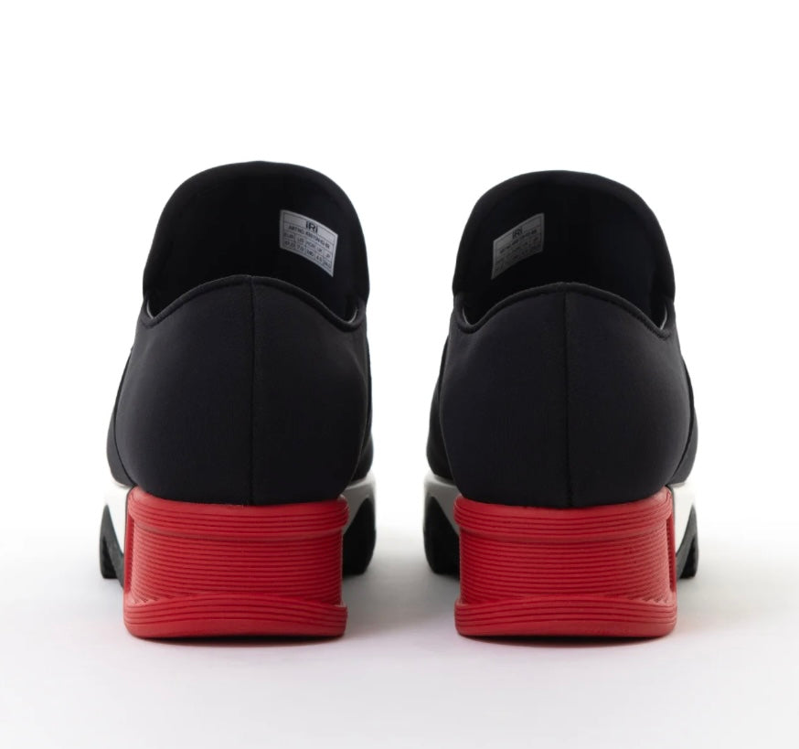 Black slip-on shoe with a red heel and black & white sole heel view