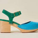 Green and blue suede shoe with golden buckle and wooden heel on a beige background