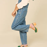 Green and blue suede clog shoe with pink strap with gold strap, and wooden sole pair on model standing with leg kicked up