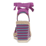 Woven wedge sandal with colorful pattern and purple bow on a white background