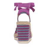 Woven wedge sandal with colorful pattern and purple bow on a white background