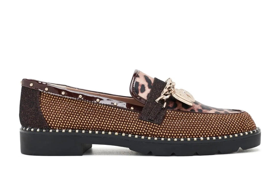 A brown loafer with a leopard print tassel strap, studded details, and a chunky black sole, shown against a plain white background.