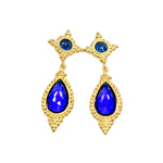 Gold colored earrings with blue teardrop stones on a white background