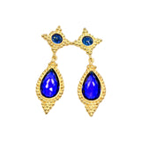 Gold colored earrings with blue teardrop stones on a white background
