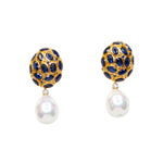 Pair of gold colored earrings with blue crystal and pearl like drop accents on a white background