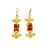 Gold colored earrings with orange stones and pearl like beads on a white background