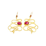 Gold colored snake shaped earrings with dark magenta stones on a white background