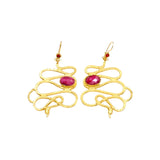 Gold colored snake shaped earrings with dark magenta stones on a white background