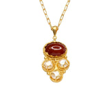 Gold colored necklace with a red stone and pearl-like accents on a gold elongated link chain on a white background